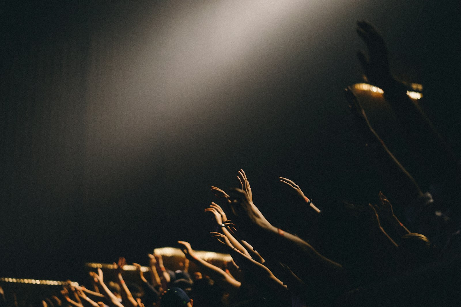 Hands raised toward a single spotlight at a concert