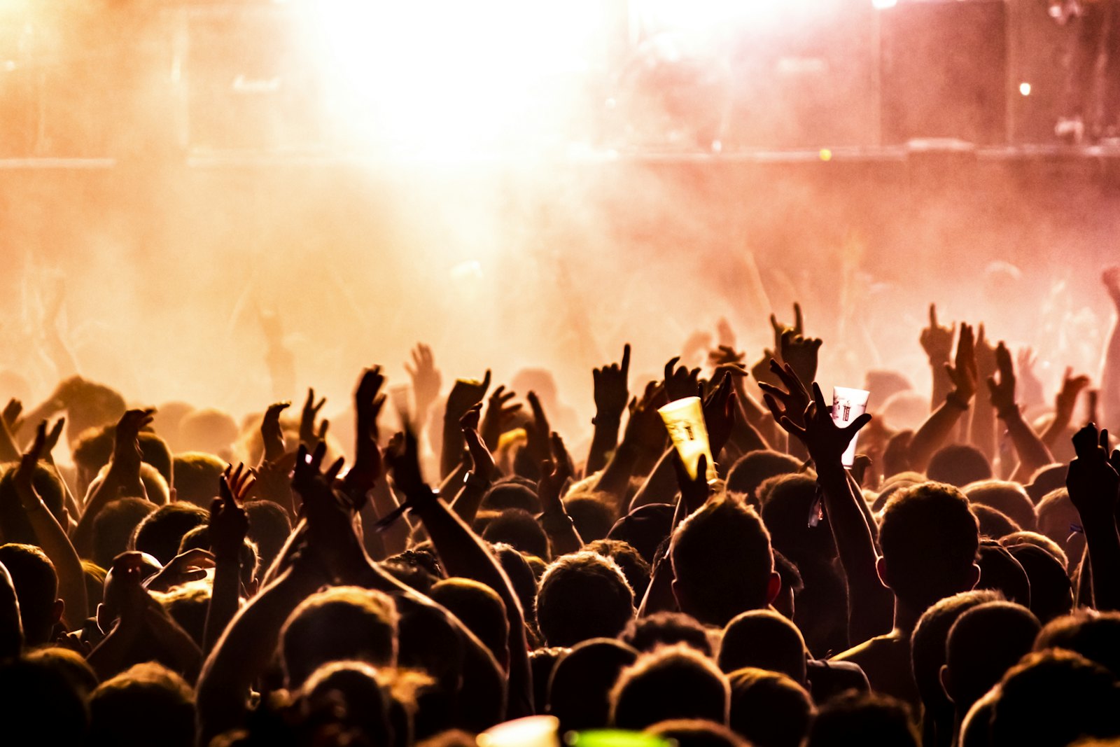 A crowd lit in warm stage light with hands in the air